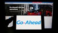 Person holding cellphone with logo of British transport company The Go-Ahead Group plc on screen in front of webpage.