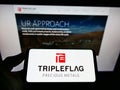 Person holding cellphone with logo of Canadian company Triple Flag Precious Metals Corp. on screen in front of webpage.