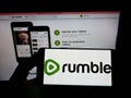 Person holding cellphone with logo of Canadian video platform company Rumble Inc. on screen in front of business webpage. Royalty Free Stock Photo