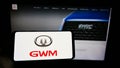 Person holding cellphone with logo of car manufacturer Great Wall Motors Co. Ltd. (GWM) on screen in front of webpage.