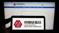 Person holding cellphone with logo of China Securities Regulatory Commission (CSRC) on screen in front of webpage.