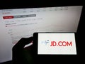 Person holding cellphone with logo of Chinese e-commerce company JD.com Inc. on screen in front of website with stock chart.