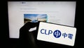 Person holding cellphone with logo of Chinese energy company CLP Group on screen in front of business webpage.
