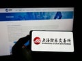 Person holding cellphone with logo of Chinese Shanghai Stock Exchange (SSE) on screen in front of business webpage.