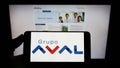 Person holding cellphone with logo of Colombian company Grupo Aval Acciones y Valores SA on screen in front of webpage. Royalty Free Stock Photo