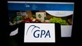 Person holding cellphone with logo of company Companhia Brasileira de DistribuiÃÂ§ÃÂ£o (GPA) on screen with webpage.