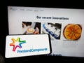 Person holding cellphone with logo of company Koninklijke FrieslandCampina N.V. on screen in front of business webpage.