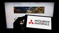 Person holding cellphone with logo of company Mitsubishi Materials Corporation (MMC) on screen in front of webpage. Royalty Free Stock Photo