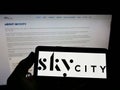 Person holding cellphone with logo of company SkyCity Entertainment Group Limited on screen in front of business webpage.