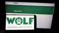 Person holding cellphone with logo of company Wolf Carbon Solutions on screen in front of business webpage.