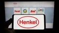 Person holding cellphone with logo of consumer goods company Henkel AG Co. KGaA on screen in front of business webpage. Royalty Free Stock Photo