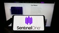 Person holding cellphone with logo of cybersecurity firm Sentinel Labs Inc. (SentinelOne) on screen in front of webpage. Royalty Free Stock Photo