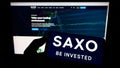 Person holding cellphone with logo of Danish investment banking company Saxo Bank AS on screen in front of webpage. Royalty Free Stock Photo