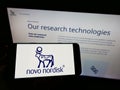 Person holding cellphone with logo of Danish pharmaceutical company Novo Nordisk AS on screen in front of business webpage. Royalty Free Stock Photo