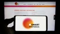 Person holding cellphone with logo of Dutch semiconductor company SMART Photonics B.V. on screen in front of webpage.