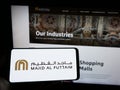 Person holding cellphone with logo of Emirati company Majid Al Futtaim Group on screen in front of business webpage.