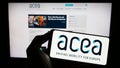 Person holding cellphone with logo of European Automobile Manufacturers Association (ACEA) on screen with webpage.