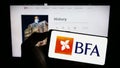 Person holding cellphone with logo of financial company Banco de Fomento Angola (BFA) on screen in front of webpage.