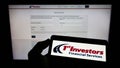 Person holding cellphone with logo of First Investors Financial Servicing Group on screen in front of business webpage.