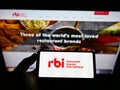 Person holding cellphone with logo of food company Restaurant Brands International Inc. (RBI) on screen with website.