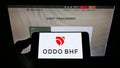 Person holding cellphone with logo of Franco-German financial company Oddo BHF AG on screen in front of business web page.