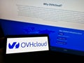 Person holding cellphone with logo of French cloud computing company OVH Groupe SAS on screen in front of business webpage.