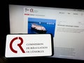 Person holding cellphone with logo of French Commission de Regulation de l\'Energie (CRE) on screen with webpage.