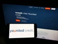 Person holding cellphone with logo of French financial platform company Younited Credit on screen in front of webpage.