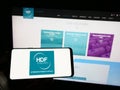 Person holding cellphone with logo of French hydrogen company HDF Energy on screen in front of business webpage.