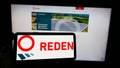 Person holding cellphone with logo of French photovoltaic company Reden Solar SAS on screen in front of business webpage.