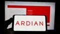 Person holding cellphone with logo of French private equity company Ardian on screen in front of business website.