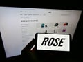 Person holding cellphone with logo of German bicycle manufacturer Rose Bikes GmbH on display in front of company website.