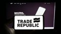 Person holding cellphone with logo of German company Trade Republic Bank GmbH on screen in front of business webpage.