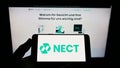 Person holding cellphone with logo of German identity verification company Nect GmbH on screen in front of business webpage. Royalty Free Stock Photo