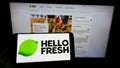 Person holding cellphone with logo of German meal-kit company HelloFresh SE on screen in front of business webpage.