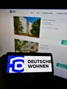 Person holding cellphone with logo of German residential property company Deutsche Wohnen on screen in front of website.