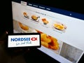 Person holding cellphone with logo of German restaurant chain Nordsee GmbH (seafood) on display in front of website.