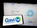 Person holding cellphone with logo of health partnership Gavi, the Vaccine Alliance on screen in front of webpage.