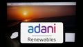 Person holding cellphone with logo of Indian company Adani Green Energy Limited on screen in front of business webpage.