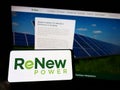 Person holding cellphone with logo of Indian company ReNew Energy Global plc on screen in front of business webpage.