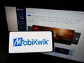 Person holding cellphone with logo of Indian financial technology company MobiKwik on screen in front of business web page.
