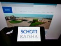 Person holding cellphone with logo of Indian packaging company Schott Kaisha Pvt Ltd on screen in front of business webpage. Royalty Free Stock Photo