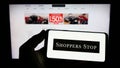 Person holding cellphone with logo of Indian retail company Shoppers Stop Limited on screen in front of business webpage.