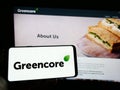 Person holding cellphone with logo of Irish food company Greencore Group plc on screen in front of business webpage.