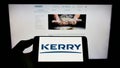Person holding cellphone with logo of Irish food company Kerry Group plc on screen in front of business webpage.
