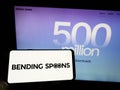 Person holding cellphone with logo of Italian app company Bending Spoons S.p.A. on screen in front of business webpage.