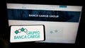 Person holding cellphone with logo of Italian bank Banca Carige SpA on screen in front of business webpage.