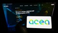 Person holding cellphone with logo of Italian utility company Acea S.p.A. on screen in front of business webpage.