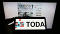 Person holding cellphone with logo of Japanese construction company Toda Corporation on screen in front of business webpage.