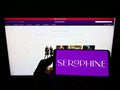 Person holding cellphone with logo of maternity fashion company Seraphine Group plc on screen in front of webpage.